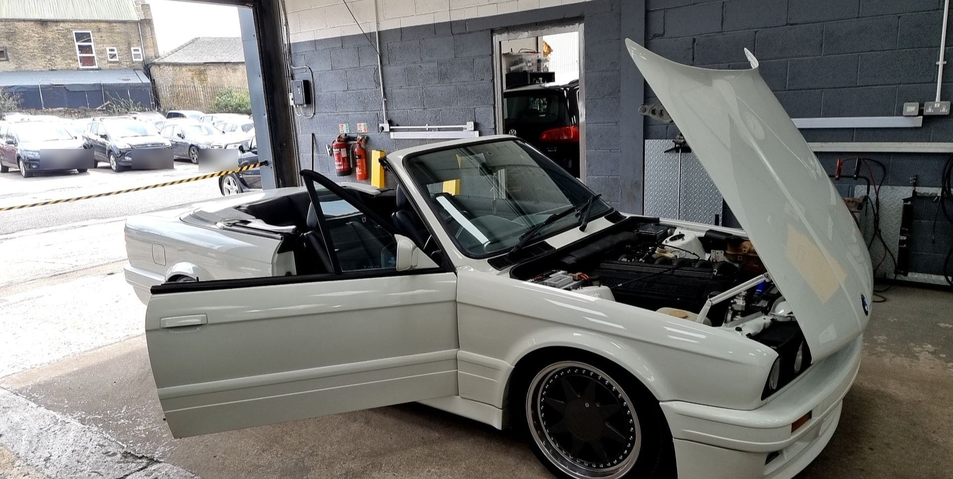 White BMW E30 convertible with the bonnet up during engine work